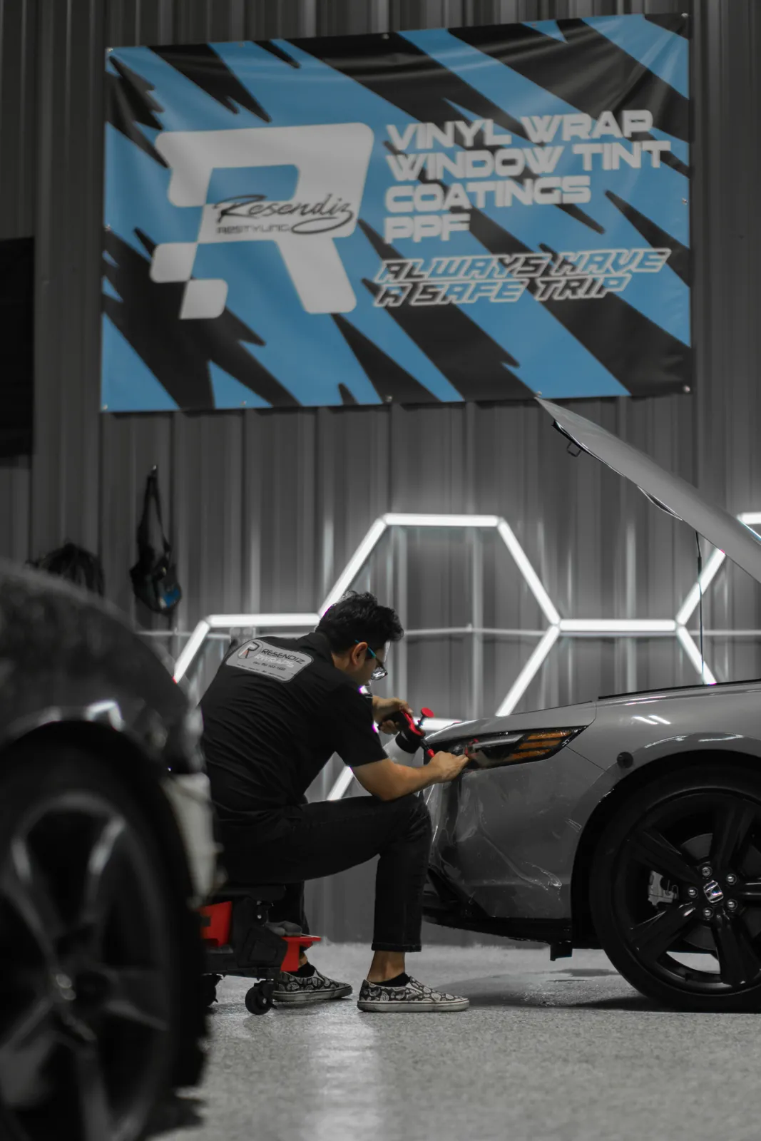 Installer working film onto a Honda front end inside the Resendiz Restyling shop, brand banner on the wall