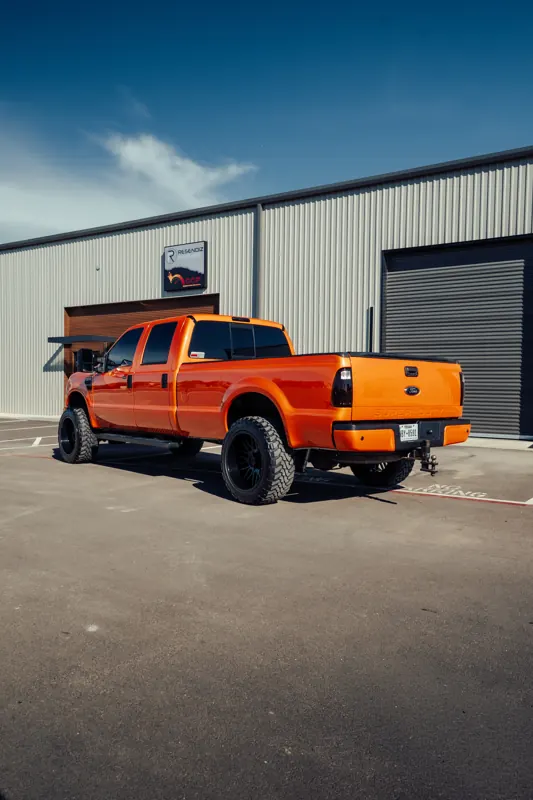Orange F-350 rear three-quarter outside the shop