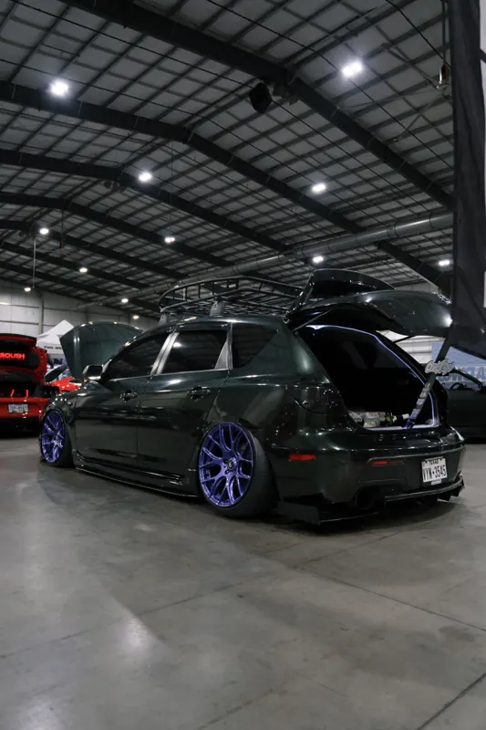 Slammed Mazda3 hatchback in dark green wrap with purple wheels